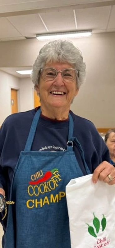 Smiling elderly woman wearing a Chili Cookoff Champ apron holding a bag.