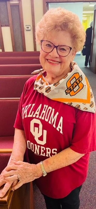 Smiling elderly woman wearing an Oklahoma Sooners shirt and an Oklahoma State scarf.