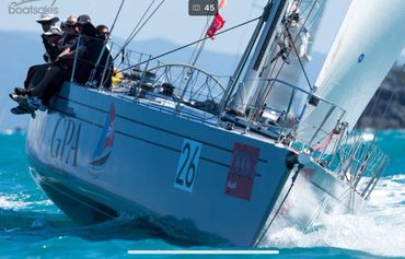 Sailing yacht with crew racing on bright blue water under clear skies.