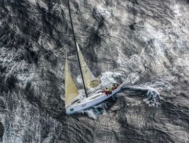 Sailboat with crew navigating choppy waters from above.