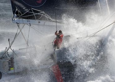 A sailor battles heavy waves on a sailboat in stormy seas.