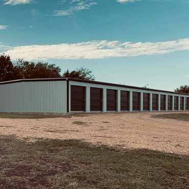 Long row of storage units with closed black doors under a blue sky.