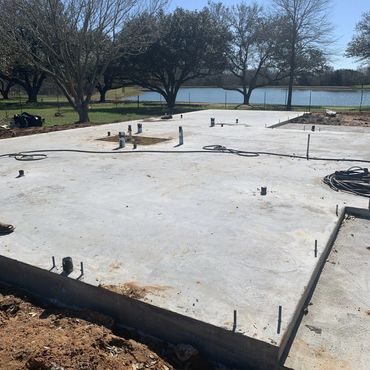 Concrete foundation slab with plumbing pipes in a sunny outdoor setting.