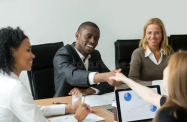 people at a table shaking hands in agreement with a laptop open