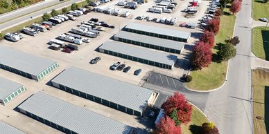 Aerial view of a storage facility with multiple rows of storage units and parked vehicles.