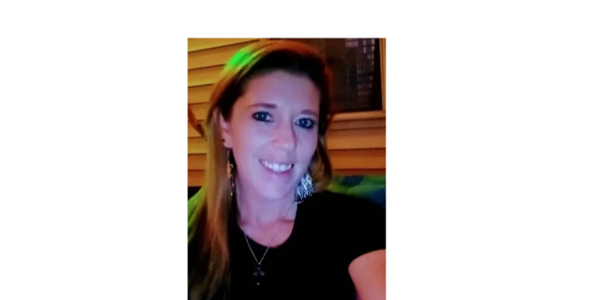 Smiling woman with long hair and earrings, sitting indoors with warm lighting.
