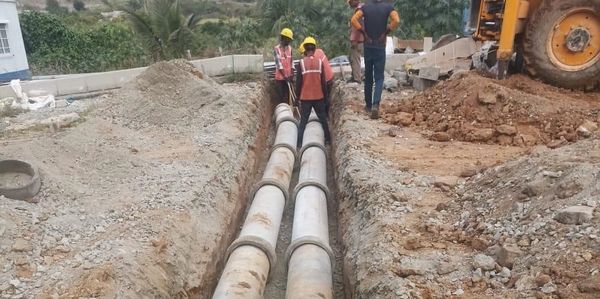 Workers installing large concrete pipes in a trench at a construction site.