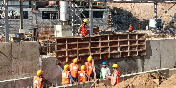 Construction workers in safety gear building a concrete structure on site.