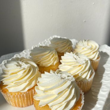 Six vanilla cupcakes with creamy swirled frosting on a white plate.