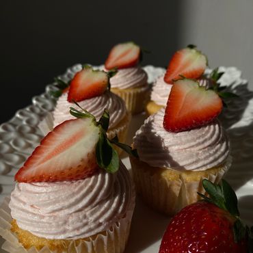 Cupcakes with pink frosting topped with fresh strawberry halves on a white plate.