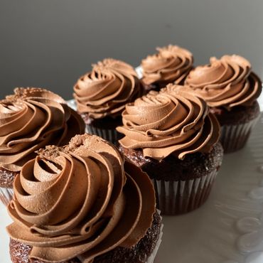 Close-up of six chocolate cupcakes with rich swirled frosting on a white plate.