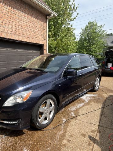 A black luxury car parked in a driveway near a brick garage.