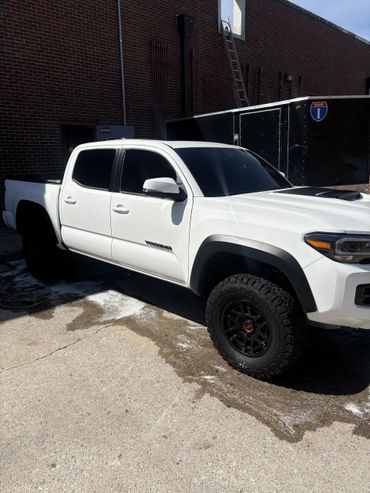 White Toyota Tacoma TRD Pro truck parked beside a black trailer and brick building.
