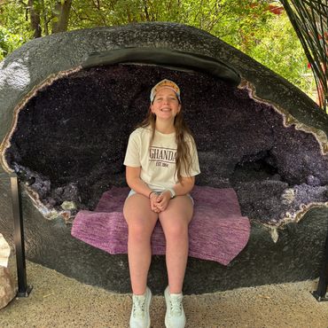 Girl smiling while sitting inside a large purple geode bench outdoors.