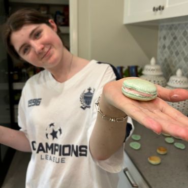 Young woman holding a green macaron with pink filling in her hand.