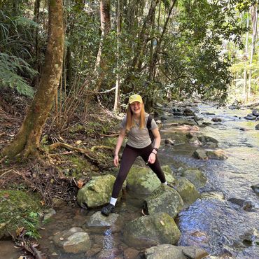 Young woman hiking and crossing a rocky stream in a forest.