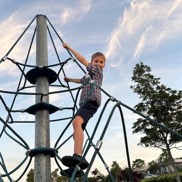A boy climbing a rope structure at a park during sunset.