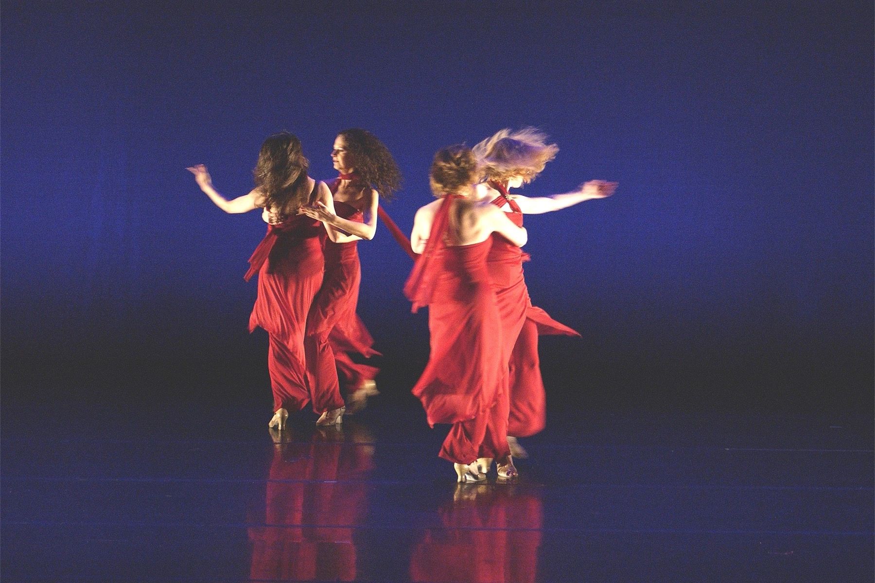 Four Tango Confusion dancers are dancing in red floating garments in front of a dark blue dreamy bac