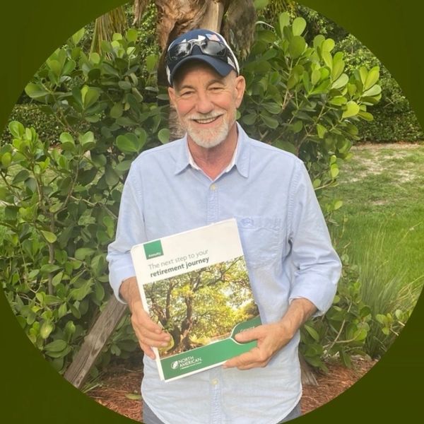 Smiling man holding a retirement guide in a lush garden.