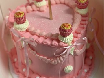 Pink heart-shaped cake decorated with Chupa Chups lollipops and ribbons.