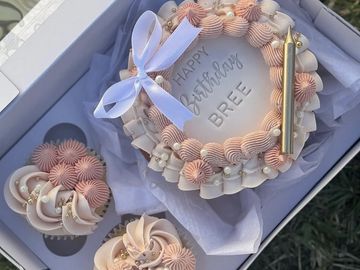 Elegant birthday cake and cupcakes with a light pink and white theme.