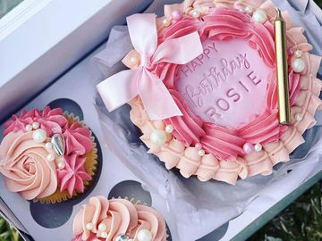 Pink birthday cake with cupcakes and decorations.