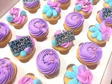 Cupcakes with purple and blue frosting, some labeled "KPOP DEMON HUNTERS".