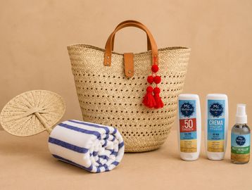 Beach essentials including a striped towel, sunscreen, cream, spray, and a woven bag.