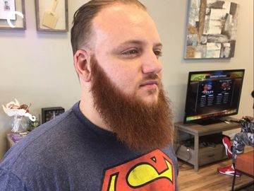 Man with a thick red beard wearing a Superman t-shirt indoors.