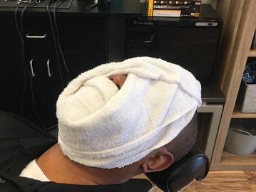 Man relaxing with a towel wrapped around his face in a barbershop chair.