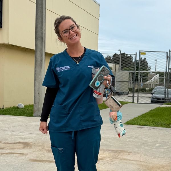Smiling woman in blue medical scrubs holding phone and keys.