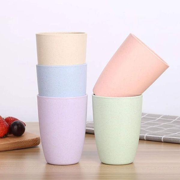 Pastel-colored cups stacked and arranged on a wooden surface with fruit on the side.