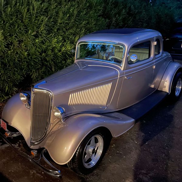 Classic silver vintage car parked near greenery at dusk.