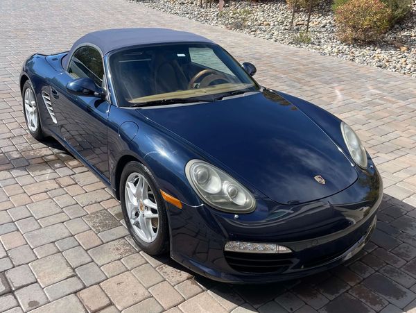 Dark blue Porsche convertible parked on a stone driveway.