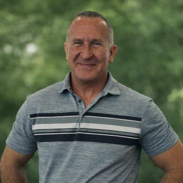 Smiling middle-aged man in a striped polo shirt outdoors.
