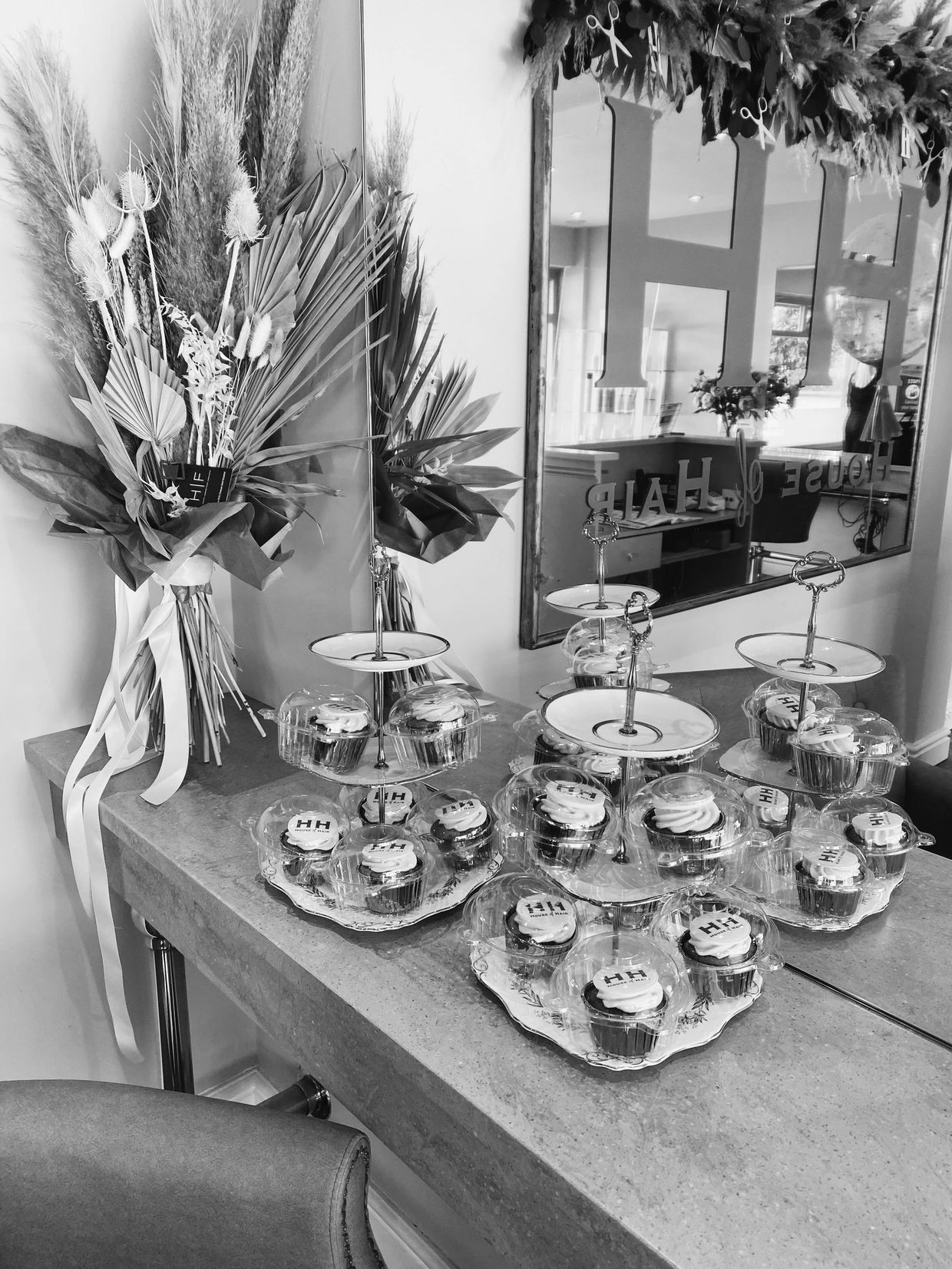 Cupcakes and dried flowers on a counter with a mirror.
