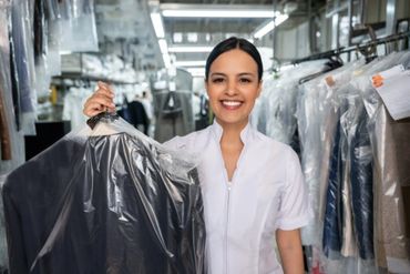 Smiling woman holding a freshly cleaned suit in a dry cleaner shop.
