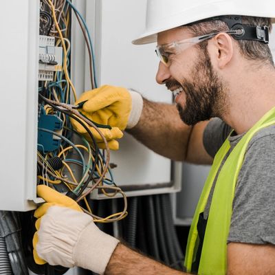 side view of smiling handsome electrician repairing electrical box with pliers in corridor