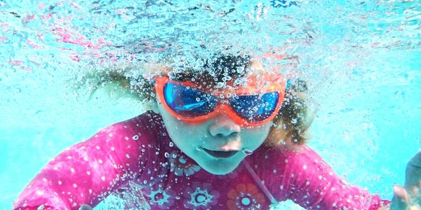 Child swimming underwater wearing orange goggles and pink swimwear.
