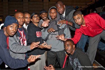 A group of young men posing together indoors, some making hand signs.