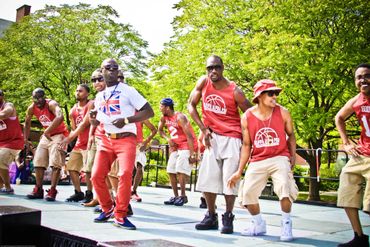 A group of men energetically dancing outdoors on a sunny day.