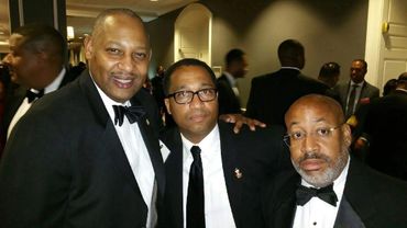Three men in tuxedos posing at a formal event.