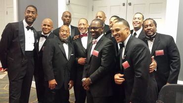 A group of men dressed in tuxedos smiling and posing together indoors.