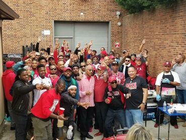 A large group of men posing and making hand signs outdoors by a brick wall.