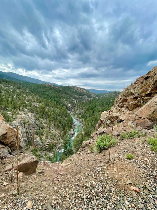 A river winding through a rocky, forested canyon under a cloudy sky.
