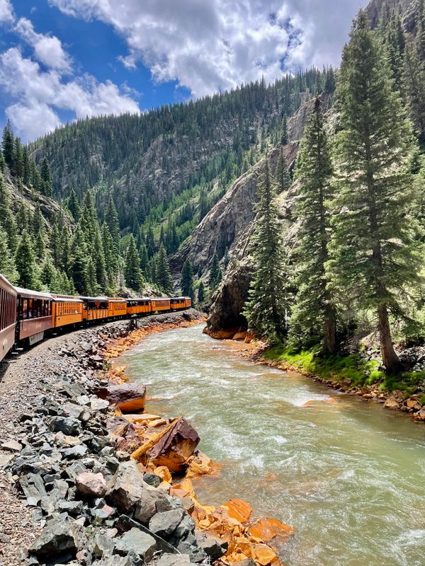 A scenic train ride along a river in a mountainous forest landscape.