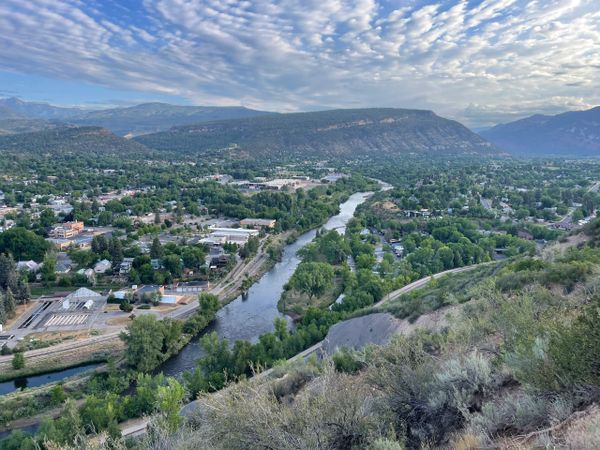 A river winding through a green valley town with mountains in the background.