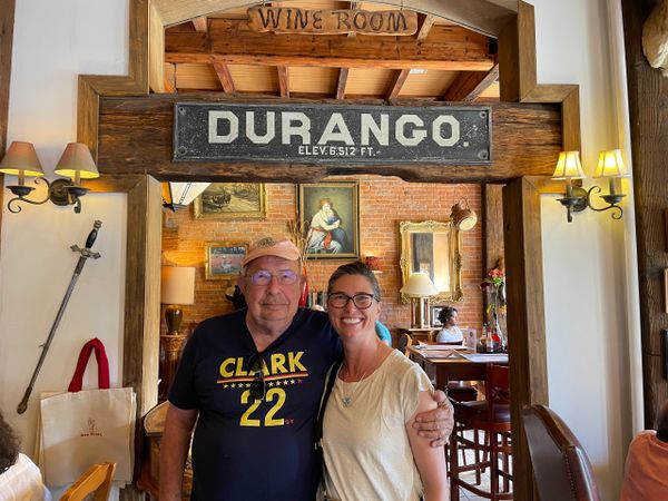An older man and a woman smiling inside a rustic restaurant under a Durango sign.