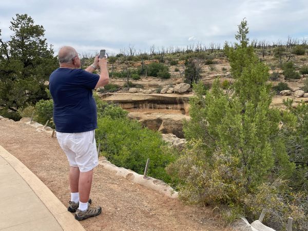 Man taking a photo of a rocky landscape with sparse vegetation.
