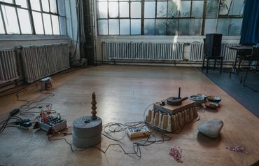 An art installation with stones, bowls, and electronic equipment in a sunlit room.